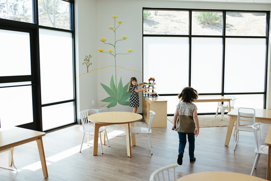 Little girl walks toward smiling girl who is holding a toy