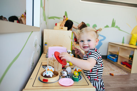 Cute Blonde Toddler Girl Smiles At Camera As She Plays With Toy Stove