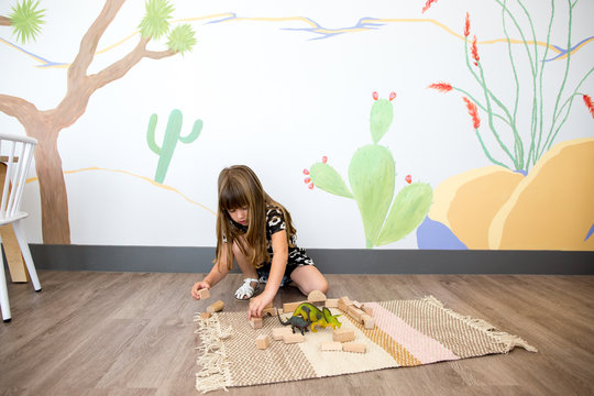 Little girl plays on the ground with blocks and dinosaurs