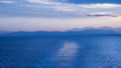 Nature in twilight period which including of sunrise over the blue water in the morning. Beautiful colorful landscape with boats, sea and purple sky. Golden light go through the cloud to the mountain 