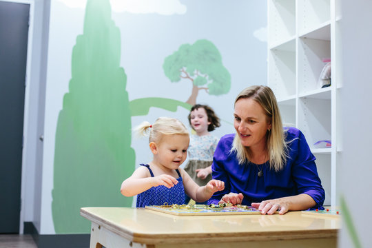 Toddler And Teacher Work Together On Puzzle At Table