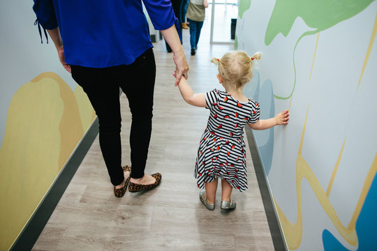 The backs of toddler girl and woman holding hands while walking