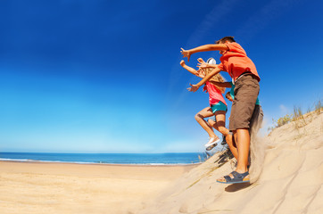 Fototapeta na wymiar Many cute children jump from sand dune hands up