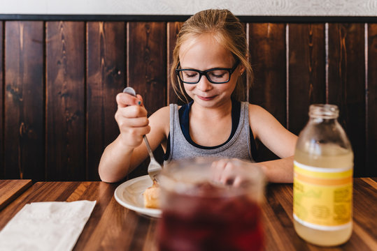 Little girl eats and drinks at table in cafe restaurant