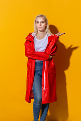 Blond girl in a red raincoat and white t-shirt standing isolated over yellow background. Be bright in bad weather.