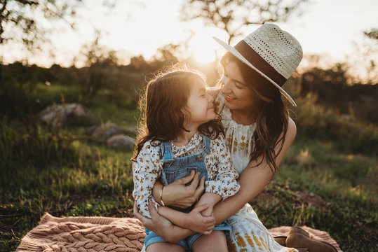 Mother and young daughter sitting on blanket in backlit meadow