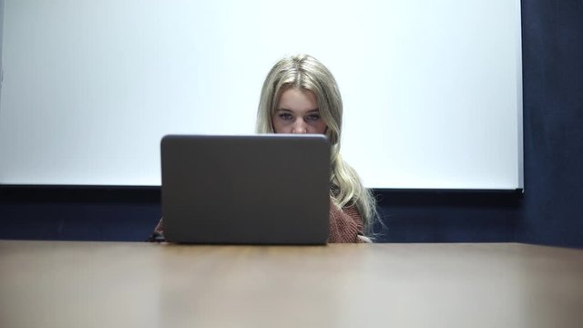 Shot of a blonde woman sitting at a table and working on her non-brand laptop.