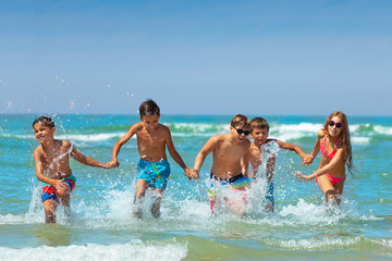 Many kids hold hands and run in the ocean water