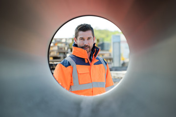 confident male engineer looking through large pipe at construction site
