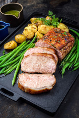 Traditionell gebratener dry aged Kalbsrücken natur mit Bohnen und Kartoffel angeboten als closeup auf einem Modern Design Tablett 