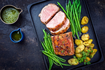 Traditional roasted dry aged veal tenderloin with beans and potatoes offered as top view on a modern design cast iron tray