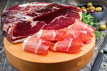 Traditioneller luftgetrockneter Parma Schinken mit Kräuter und Oliven angeboten als closeup auf...