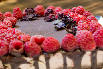Sweet present for lovers. Harmless sweeties. Close up chocolate vegan cake with raspberries on white plate on wooden background.