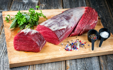 Dry aged beef fillet steak natural offered as closeup with spice and salt on a wooden cutting board