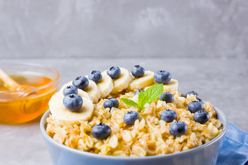 Oatmeal with berries and nuts. Breakfast: oatmeal, blueberries, banana and honey. Cooked oatmeal in bowl on blue napkin