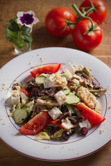 Tomato, cucumber, lettuce and mushroom salad with feta cheese, walnuts and grapes on white plate, wooden table