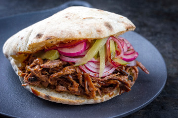 Traditional barbecue pulled beef burger offered with Carolina BBQ sauce, gherkin and onion rings as...