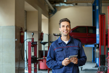 Naklejka na ściany i meble Male mechanic with tablet computer in car service center