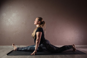 Young sporty attractive woman practicing yoga, meditating in yoga pose, working out, wearing sportswear, indoor full length, brown yoga studio