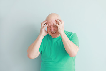 Senior man suffering from headache on light background