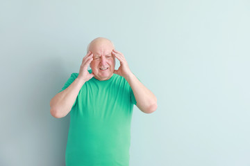 Senior man suffering from headache on light background