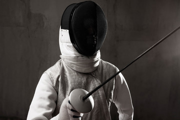 Portrait of male fencer in mask and foil performing fight in studio, dark key