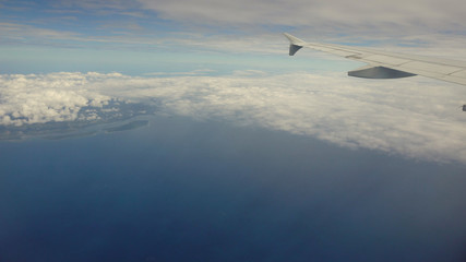 Blue sea or ocean in it and small tropical islands. Looking through window aircraft during flight