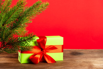Christmas composition. Green gift box under the Christmas tree on a wooden table near a red background. a Christmas gift