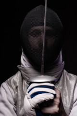 Portrait of male fencer in mask and foil performing fight in studio, dark key