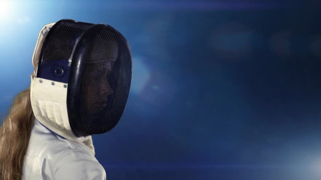 Fencer puts on mask and becomes fencing combat stance. Sport girl fencer with epee before competition in fencing hall with light background.