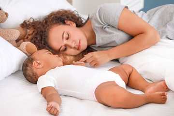 Young African-American woman and her baby sleeping on bed