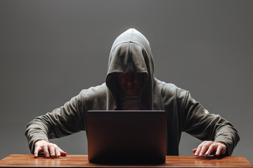 Hacker in a hood with a laptop on a dark background