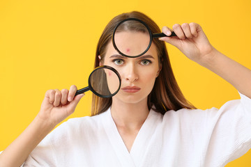 Portrait of young woman with acne problem and magnifying glasses on color background
