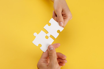 cropped view of woman and man matching pieces of white puzzle on yellow background