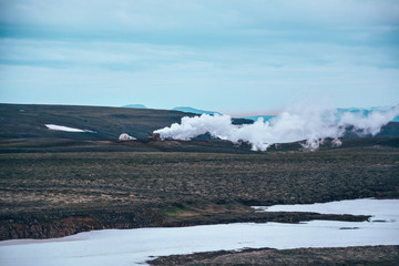 Leirhnjukur old black lava field with snow and colorful stones and smoke coming from ground and blue sky in Iceland, overcast day in summer , film effect with grain