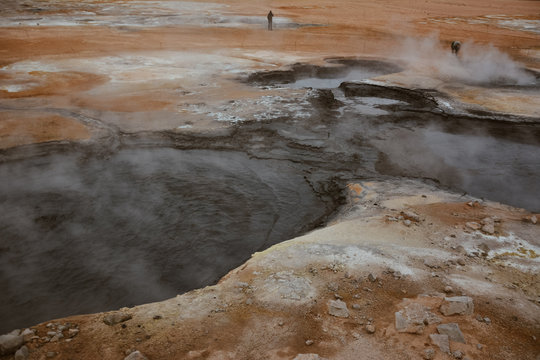 Boiling mudpots in the geothermal area Hverir and cracked ground around with unrecognisable tourists, Iceland in summer. Myvatn region, North part of Iceland