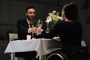 back view of disabled young woman clinking glasses of red wine with handsome boyfriend during romantic dinner