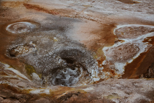 Closeup of solfatare mudpot s in the geothermal area Hverir, Iceland. The area around the boiling mud is multicolored and cracked.