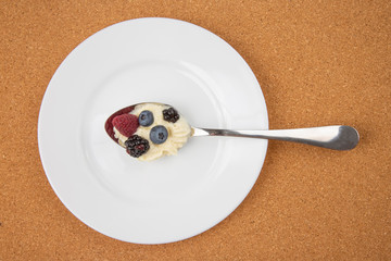 Raspberries, blackberries, blueberries with cream in a spoon on a white plate. Vitamins and Nutrition