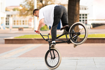 The guy on the BMX bike performs a trick on the front wheel.