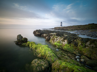 A lighthouse with algae covered rocks in the foreground