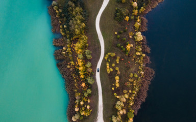 Black car between two different color lakes from drone