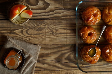 Baked in the oven with honey apples in a glass bowl with a spoon of honey, half a fresh Apple in a ceramic saucepan and a jar of honey on a textured napkin stand on a wooden background top view.