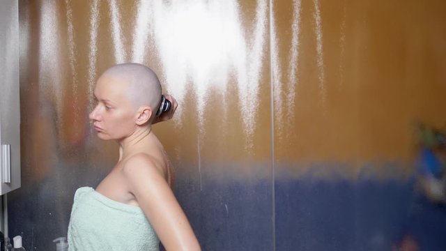a bald woman shaves her head in the bathroom after a shower. Copy space. adventures of strange people