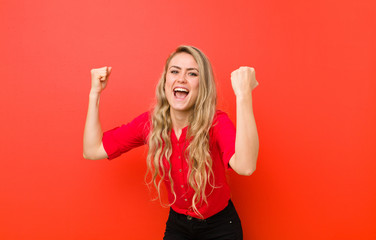 young blonde woman shouting triumphantly, looking like excited, happy and surprised winner,...