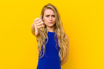 young blonde woman feeling cross, angry, annoyed, disappointed or displeased, showing thumbs down with a serious look against yellow wall © kues1