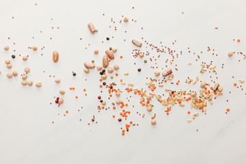 top view of scattered beans, lentil, oatmeals and peppercorns on marble surface