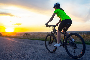 Fototapeta na wymiar Beautiful girl cyclist rides a bicycle on the road in the sunset. Healthy lifestyle and sport. Leisure and hobbies