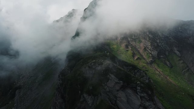 Aerial view; drone flying to mount peak through the thick clouds; natural beauty of Caucasus mountain ridge; steep stony slope and rocky cliffs; dangerous tracking routes; touristic city Sochi, Russia