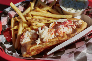 Eating traditional Maine lobster roll with coleslaw and French fries on a waterfront harbor in Maine.  